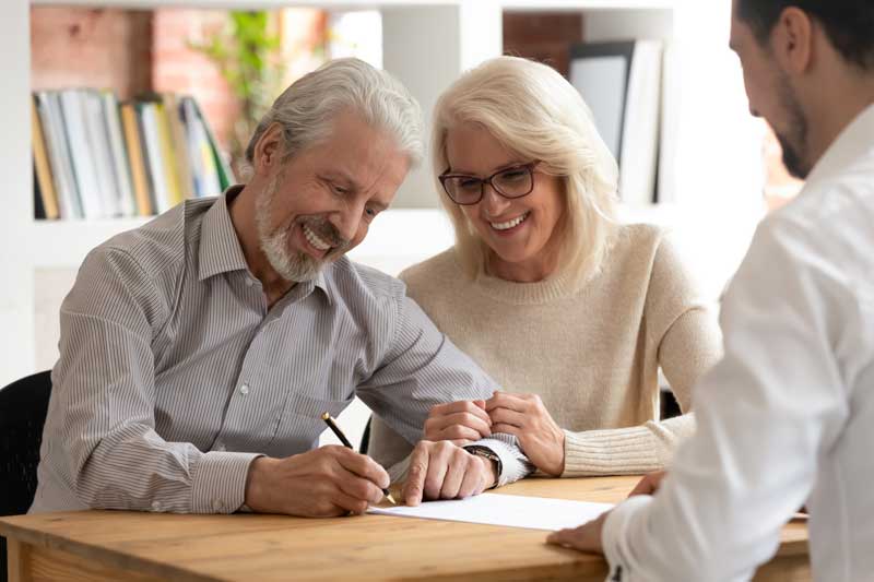 probate lawyer massachusetts - Photo description: smiling senior couple signing documents, meeting with attorney.