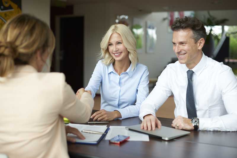 probate litigation attorney massachusetts - Photo description: Shot of an investment manager shaking hands with smiling woman while consulting with middle aged couple about financial savings.